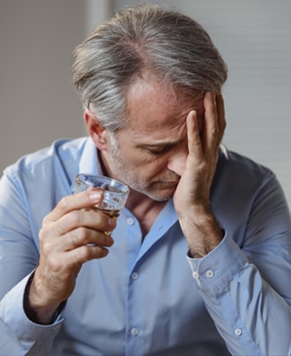 Alcool et sclérose en plaques : homme senior qui se sent mal avec un verre à la main.